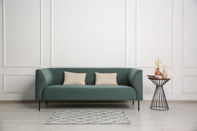 Stylish sofa, pillows and side table with decor near white wall indoors