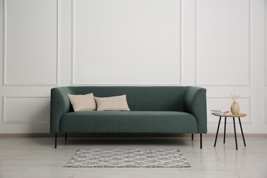 Photo of Stylish sofa, pillows and side table with decor near white wall indoors