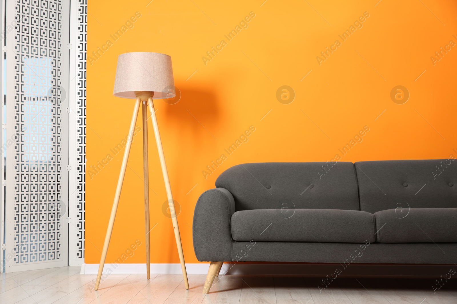 Photo of Stylish sofa and lamp near orange wall indoors