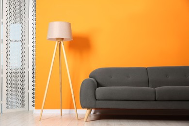 Photo of Stylish sofa and lamp near orange wall indoors