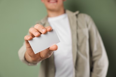 Man holding blank business card on green background, closeup. Mockup for design