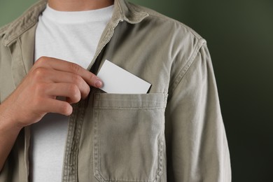 Photo of Man taking blank business card from pocket of his jacket on green background, closeup. Mockup for design