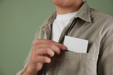 Photo of Man taking blank business card from pocket of his jacket on green background, closeup. Mockup for design