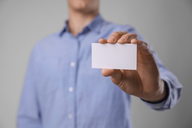 Man holding blank business card on grey background, closeup. Mockup for design