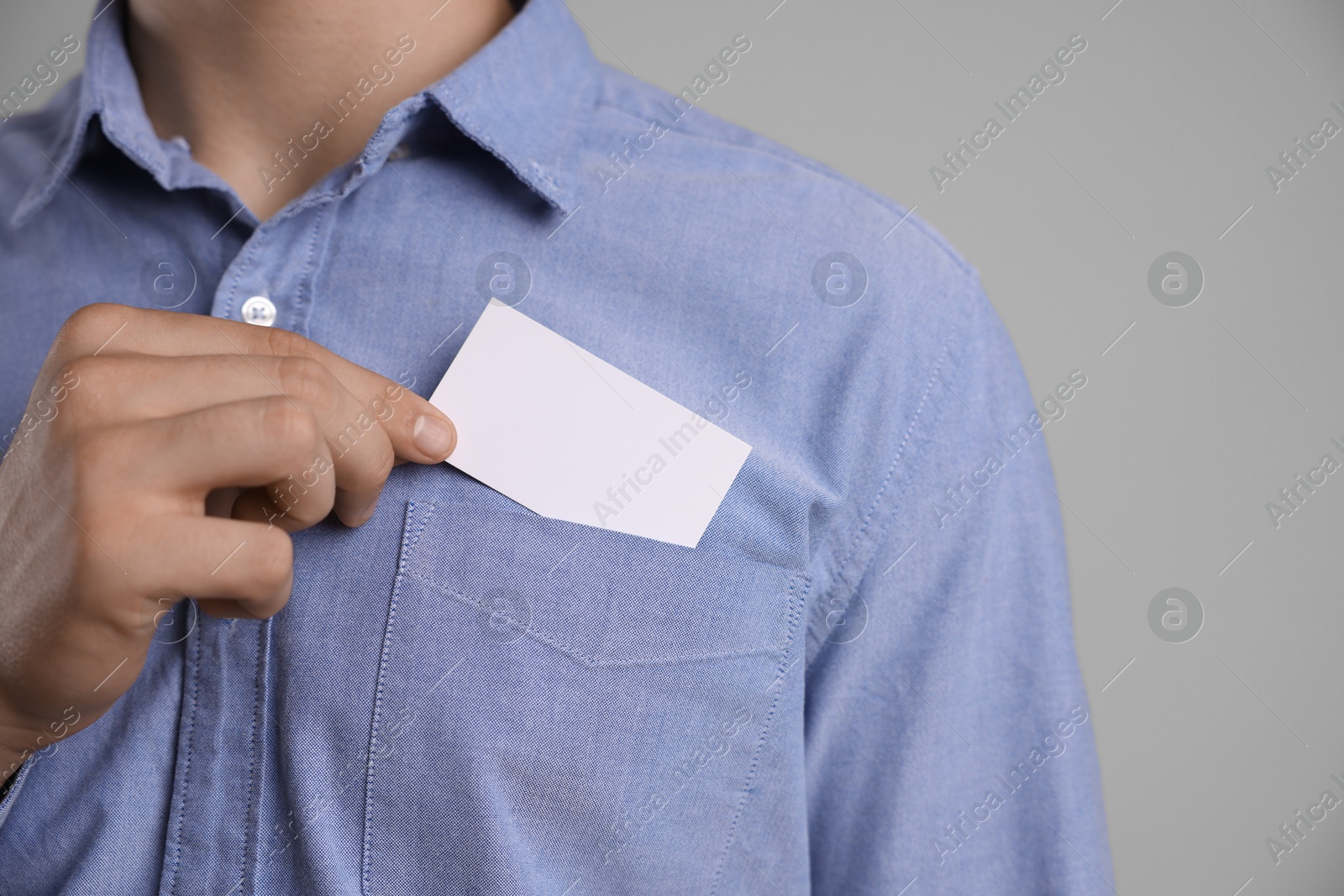 Photo of Man taking blank business card from pocket of his jacket on grey background, closeup. Mockup for design