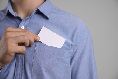 Man taking blank business card from pocket of his jacket on grey background, closeup. Mockup for design