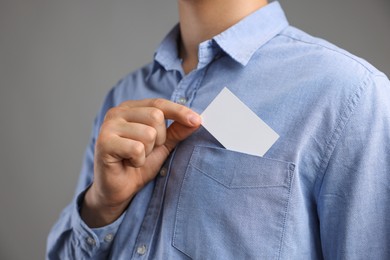 Photo of Man taking blank business card from pocket of his jacket on grey background, closeup. Mockup for design