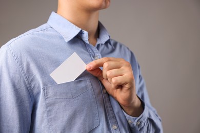 Man taking blank business card from pocket of his jacket on grey background, closeup. Mockup for design