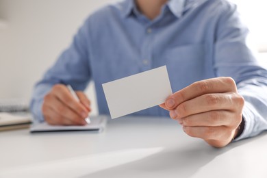 Photo of Man holding blank business card at table in office, closeup. Mockup for design