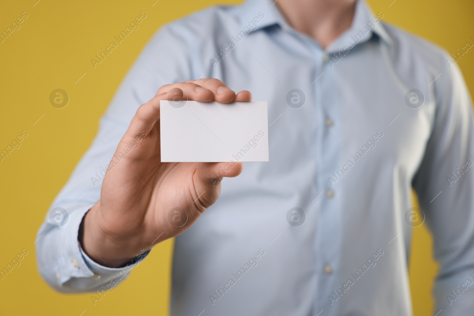 Photo of Man holding blank business card on yellow background, closeup. Mockup for design