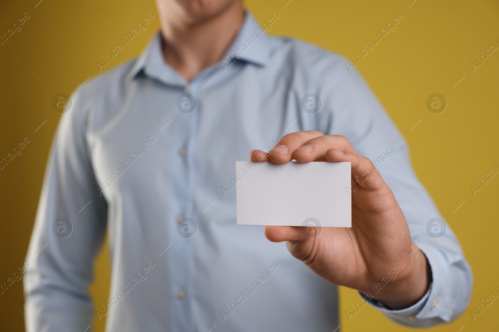 Photo of Man holding blank business card on yellow background, closeup. Mockup for design