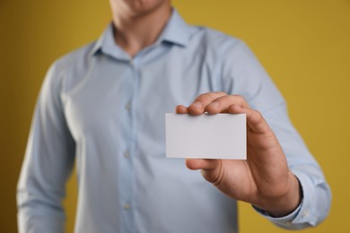 Photo of Man holding blank business card on yellow background, closeup. Mockup for design