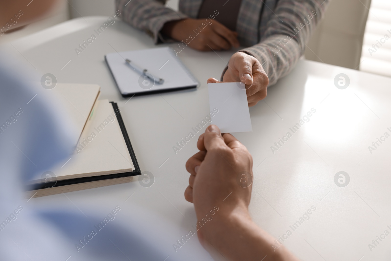 Photo of Woman giving business card to man at table in office, closeup. Mockup for design