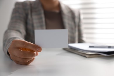 Woman holding blank business card at table in office, closeup. Mockup for design