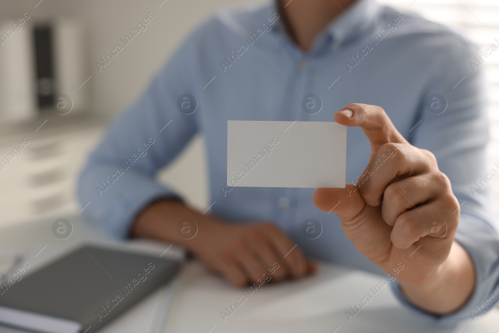 Photo of Woman holding blank business card at table in office, closeup. Mockup for design