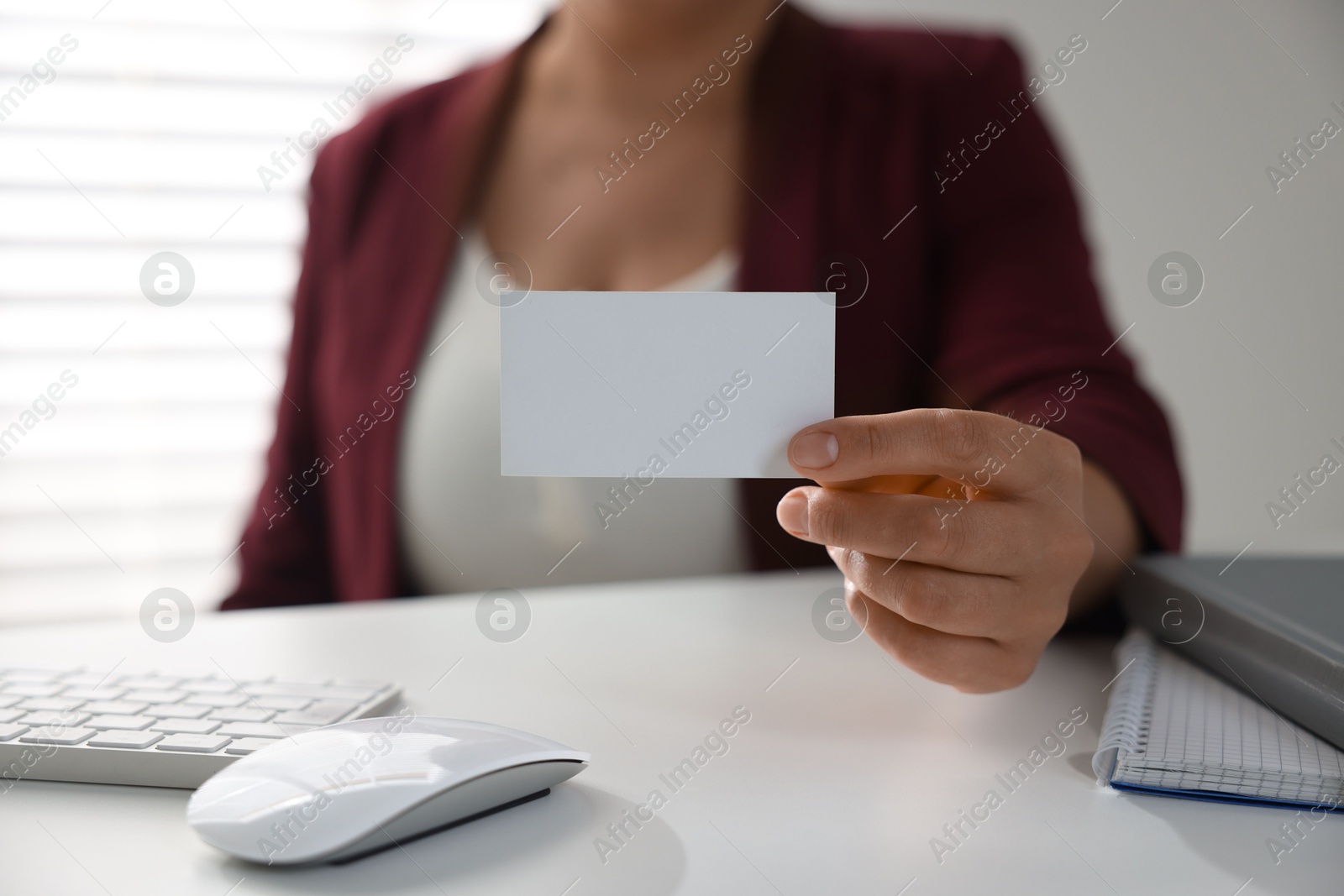 Photo of Woman holding blank business card at table in office, closeup. Mockup for design