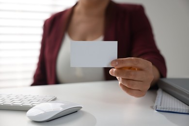 Woman holding blank business card at table in office, closeup. Mockup for design