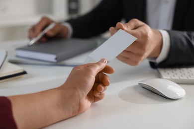 Woman giving business card to man at table in office, closeup. Mockup for design