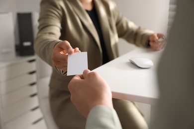 Photo of Woman giving business card to man at table in office, closeup. Mockup for design