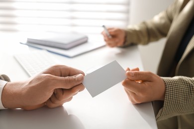 Man giving business card to woman at table in office, closeup. Mockup for design