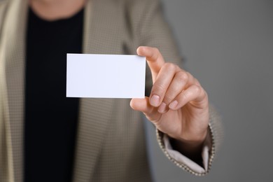 Woman holding blank business card on grey background, closeup. Mockup for design