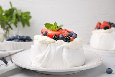 Photo of Pavlova cake (meringue dessert) with whipped cream, fresh berries and mint on white table, closeup