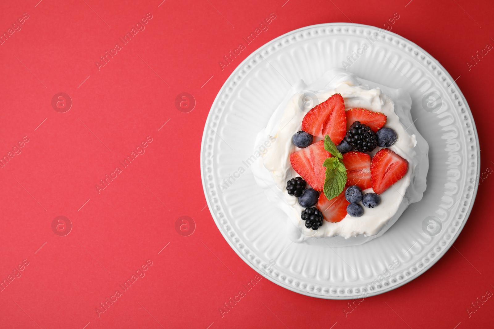 Photo of Pavlova cake (meringue dessert) with whipped cream, fresh berries and mint on red background, top view. Space for text