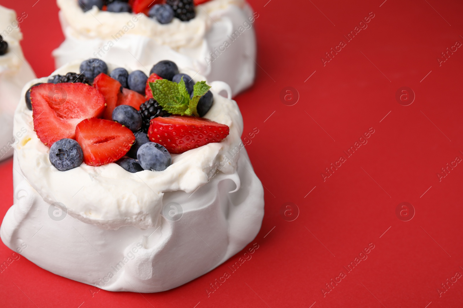 Photo of Pavlova cake (meringue dessert) with whipped cream, fresh berries and mint on red background, closeup. Space for text