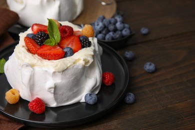 Photo of Pavlova cake (meringue dessert) with whipped cream, fresh berries and mint on wooden table, closeup