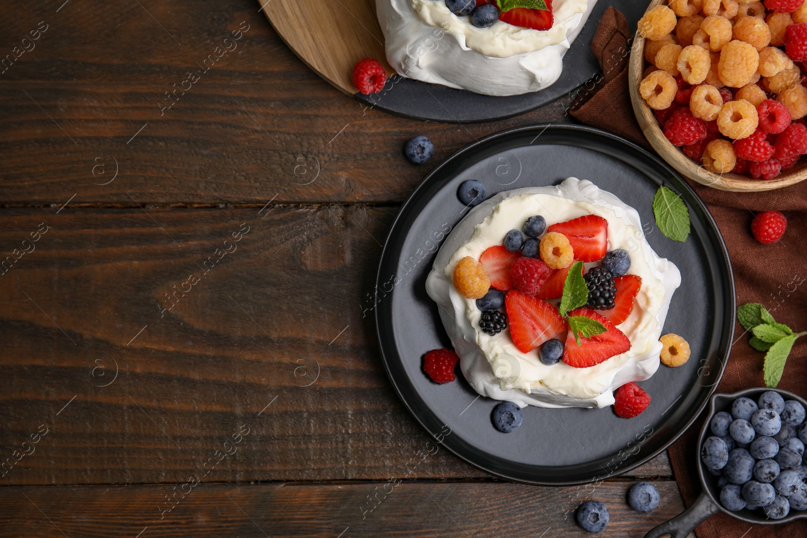 Photo of Pavlova cake (meringue dessert) with whipped cream, fresh berries and mint on wooden table, flat lay. Space for text