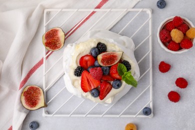 Photo of Pavlova cake (meringue dessert) with whipped cream, fresh berries, mint and fig on light grey table, flat lay