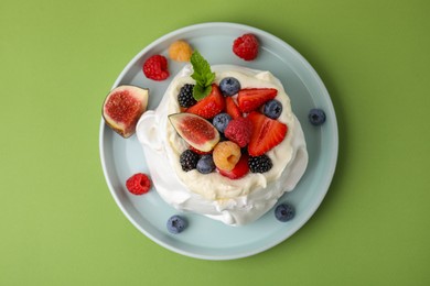 Photo of Pavlova cake (meringue dessert) with whipped cream, fresh berries, mint and fig on green background, top view