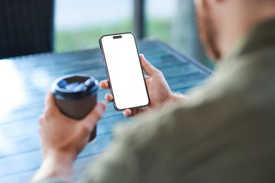 Man with paper cup using smartphone at outdoor cafe, closeup. Space for design