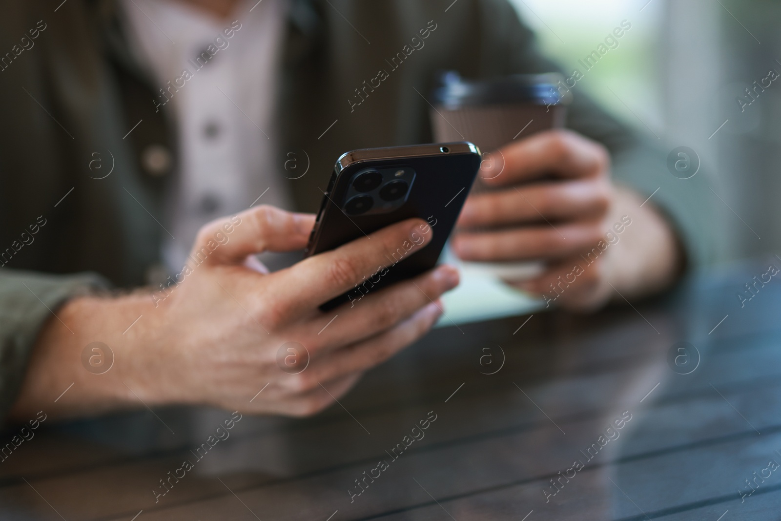 Photo of Man with paper cup using smartphone at outdoor cafe, closeup