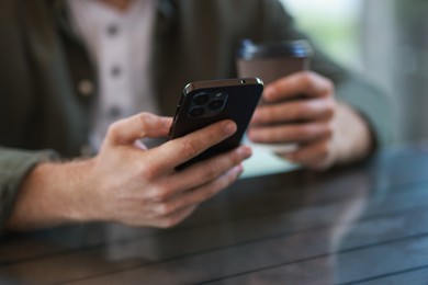 Photo of Man with paper cup using smartphone at outdoor cafe, closeup