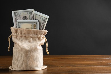 Dollar banknotes in burlap sack on wooden table against dark background, space for text