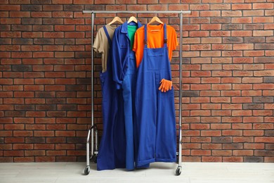 Different workers' uniforms on clothing rack near brick wall