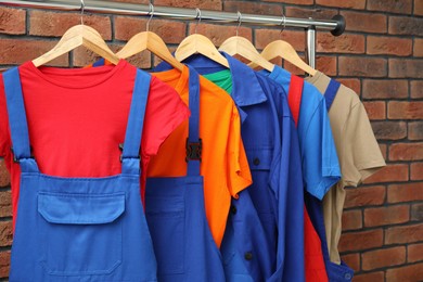 Different workers' uniforms on clothing rack near brick wall