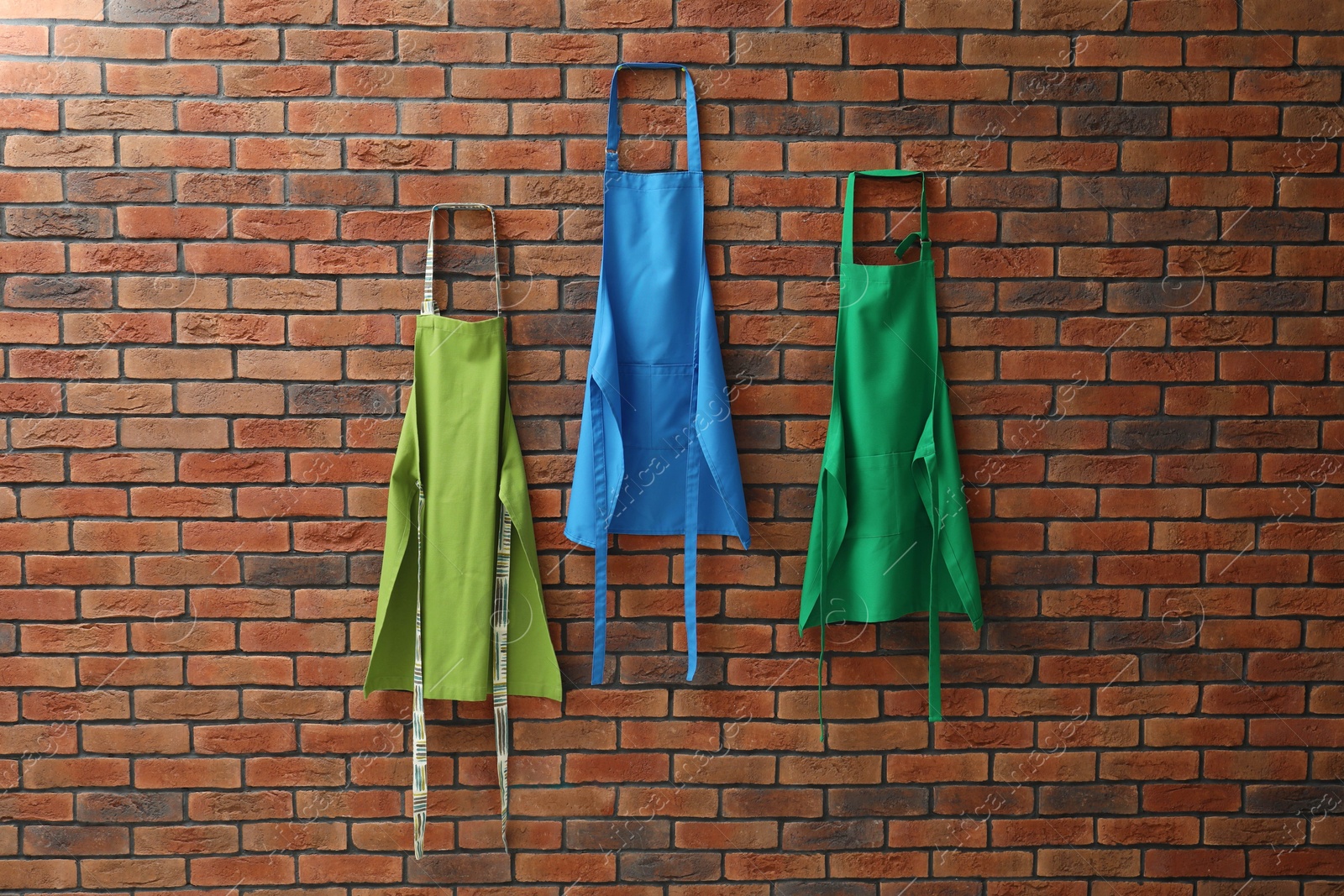 Photo of Many chef's aprons hanging on brick wall