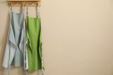 Photo of Two chef's aprons hanging on beige wall, space for text