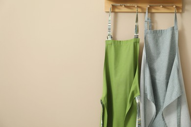 Photo of Two chef's aprons hanging on beige wall, space for text