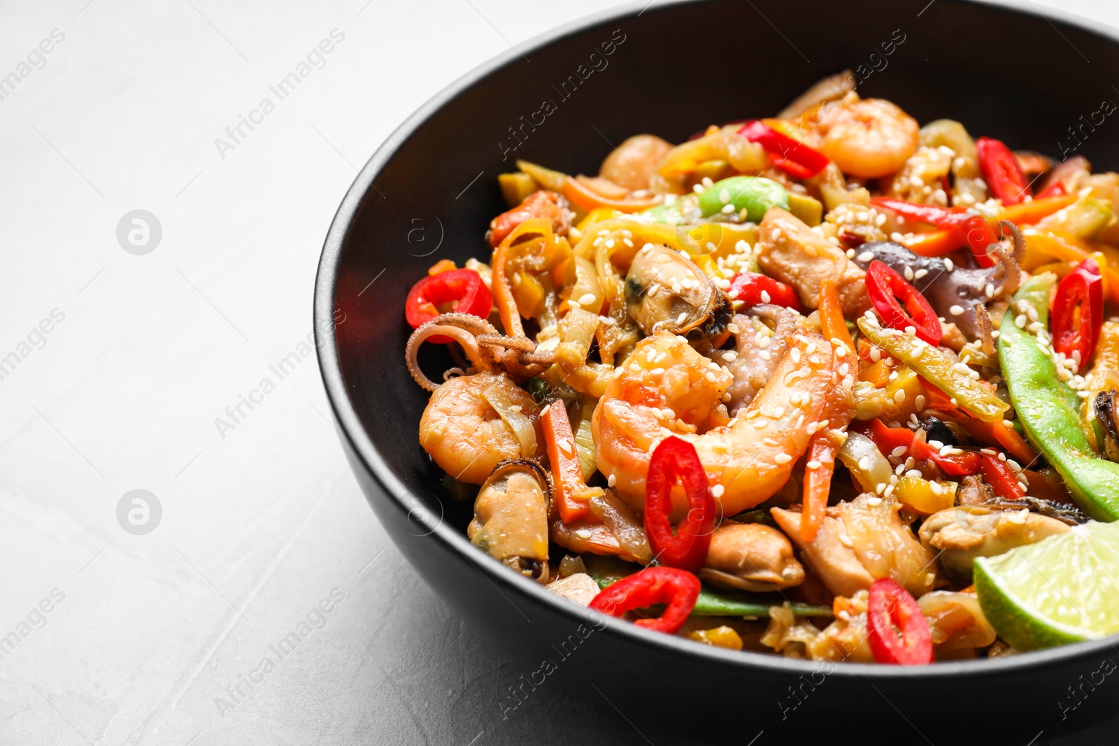 Photo of Stir-fry sea food in bowl on light grey table, closeup