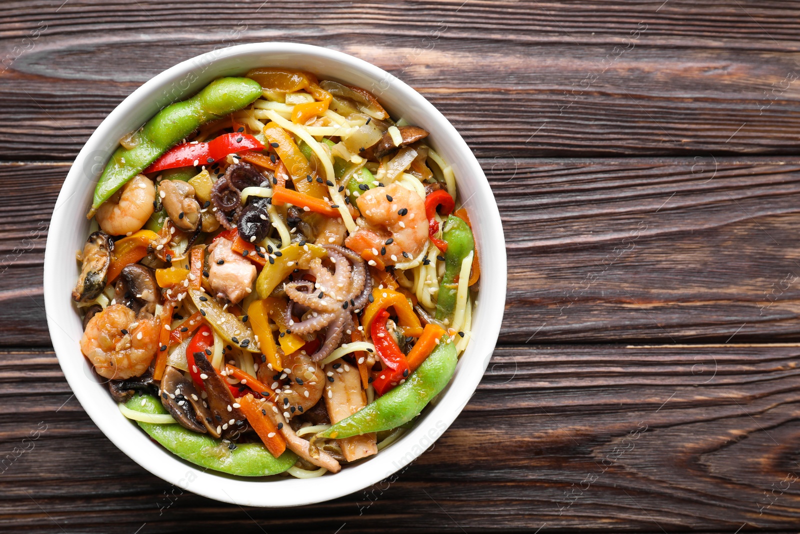 Photo of Stir-fry noodles with sea food in bowl on wooden table, top view. Space for text