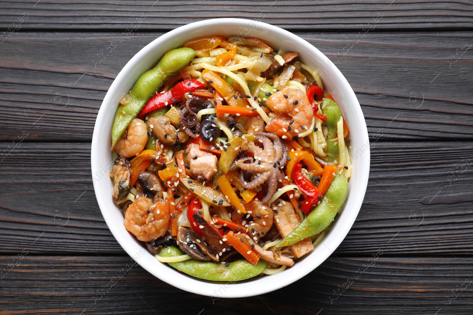 Photo of Stir-fry noodles with sea food in bowl on wooden table, top view