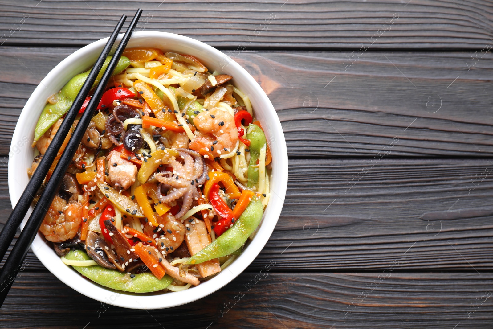 Photo of Stir-fry noodles with sea food in bowl and chopsticks on wooden table, top view. Space for text