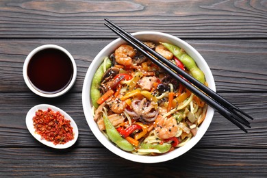 Photo of Stir-fry noodles with sea food served on wooden table, flat lay