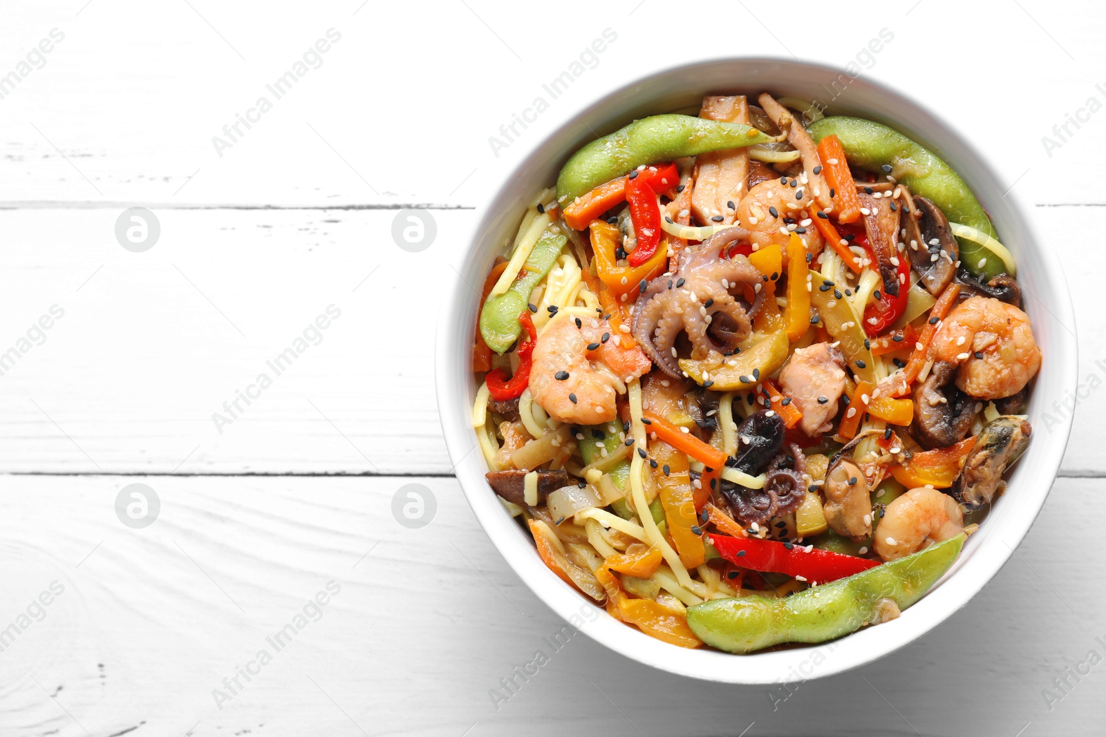 Photo of Stir-fry noodles with sea food in bowl on white wooden table, top view. Space for text