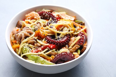 Photo of Stir-fry noodles with sea food in bowl on light grey table, closeup