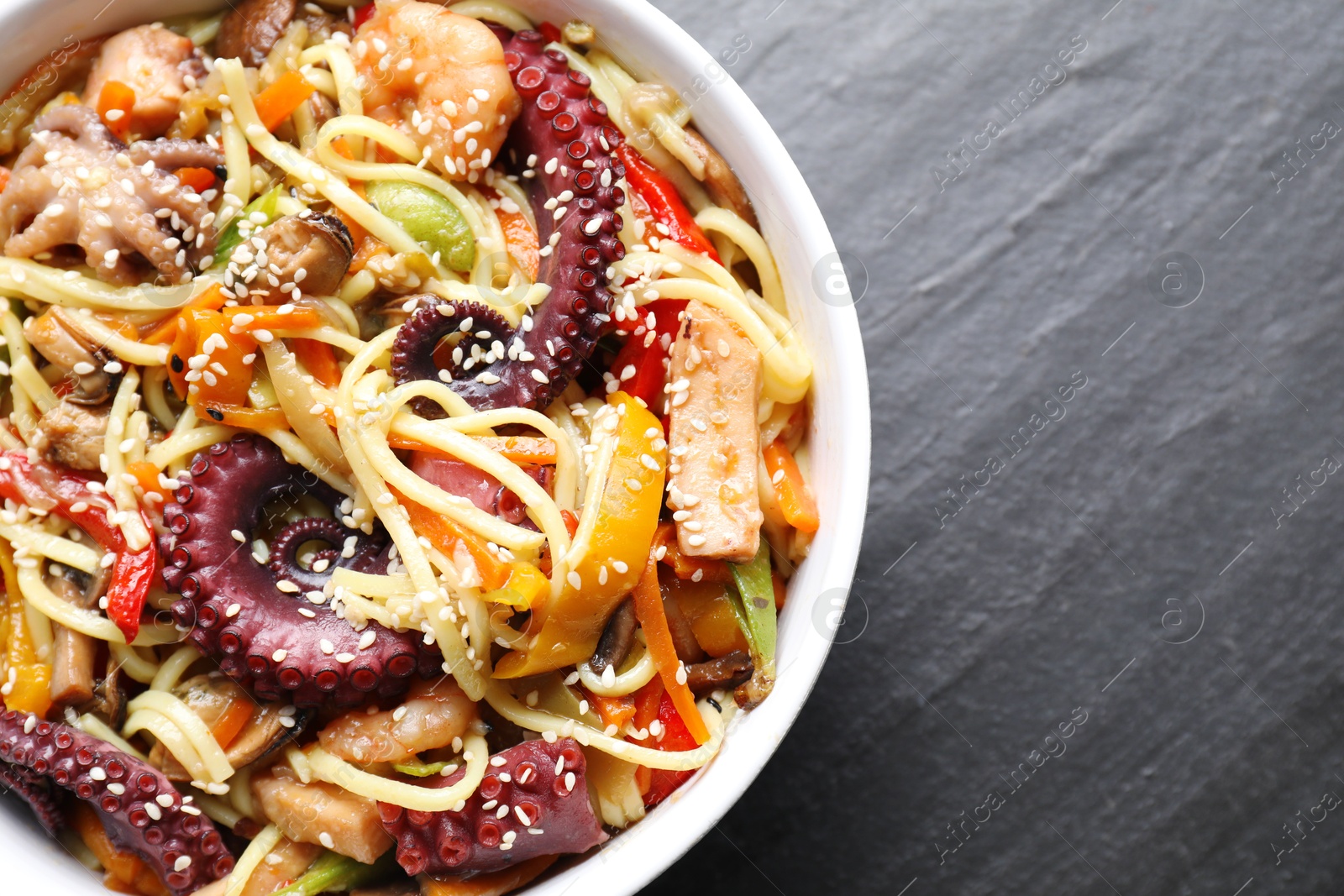 Photo of Stir-fry noodles with sea food in bowl on grey textured table, top view. Space for text