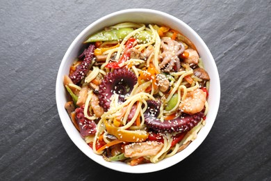 Photo of Stir-fry noodles with sea food in bowl on grey textured table, top view